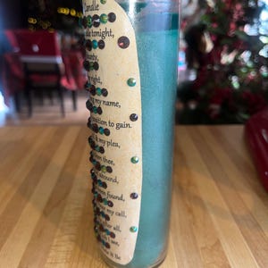 May include: A teal green candle with a label that reads "Candle tonight, munty, right, my name, position to gain. my plea, en thee, abound, en found, my call. fter all, ... Make it Be". The label is decorated with small, colorful rhinestones.