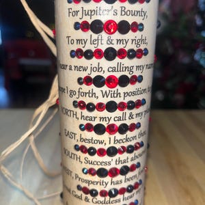 May include: A beige candle with a red and black design. The candle has a text inscription that reads: "set aflame this candle tonight For Jupiter's Bounty, To my left & my right, I hear a new job, calling my name. Hope I go forth, With position to WORTH, hear my call & my place EAST, bestow, I beckon there SOUTH, Success' that abounds WEST, Prosperity has been found. Let God & Goddess hear my plea A new path before me after this. Thank You for this job."