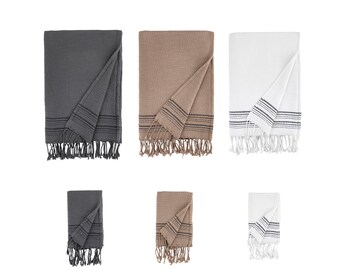 Puede incluir: Tres mantas de tiro rayadas de diferentes colores con flecos. Las mantas están dobladas por la mitad y colocadas sobre un fondo blanco. Los colores son gris, marrón y blanco.