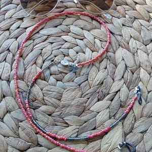 May include: Sunglasses with a beaded eyeglass chain. The chain is primarily red and pink with a section of gray beads. The sunglasses have a silver frame and dark lenses. The chain has a small silver charm with a flower.