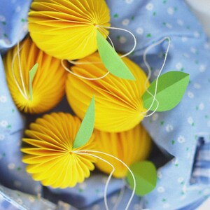 May include: A blue fabric bag with white polka dots holds five yellow paper honeycomb balls with green paper leaves attached.