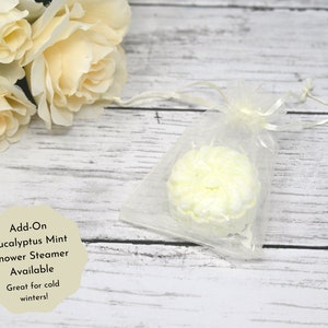 May include: A white shower steamer in a clear organza bag. The steamer is shaped like a flower and has a light green tint. The text "Add-On Eucalyptus Mint Shower Steamer Available Great for cold winters!" is written on a white background.