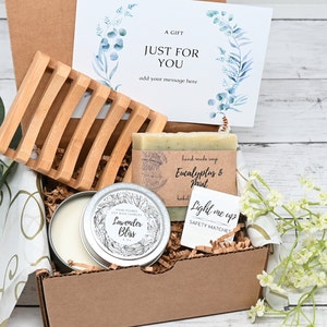 May include: A gift box filled with self-care items, including a candle, soap, matches, and a soap dish. The box is decorated with a card that says "A Gift Just For You" and has a floral design.