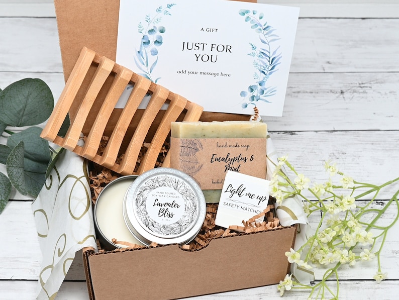 May include: A gift box filled with self-care items, including a candle, soap, matches, and a soap dish. The box is decorated with a card that says "A Gift Just For You" and has a floral design.