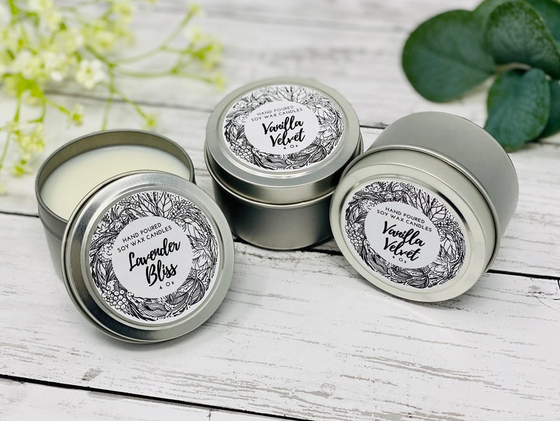 May include: Three silver candle tins with black and white labels. The labels feature a floral design and the text "Hand Poured Soy Wax Candles". The candles are labeled "Lavender Bliss", "Vanilla Velvet", and "Vanilla Velvet".