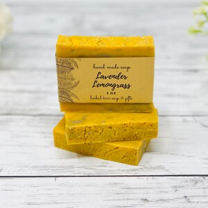 May include: Three bars of handmade yellow soap stacked on top of each other. The top bar has a brown paper label that reads "hand made soap Lavender Lemongrass 1 oz herbal kiwi soap & gifts".