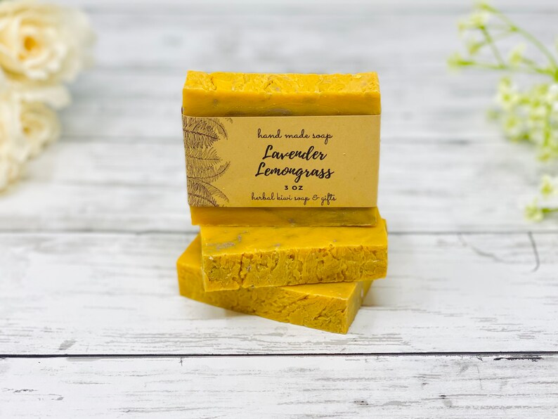 May include: Three bars of handmade yellow soap stacked on top of each other. The top bar has a brown paper label that reads "hand made soap Lavender Lemongrass 1 oz herbal kiwi soap & gifts".