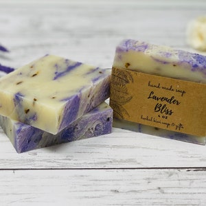 May include: Two bars of lavender-colored soap with a brown label that reads "hand made soap Lavender Bliss 4 oz herbal bliss soap & gifts".