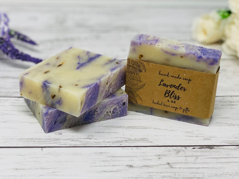 May include: Two bars of lavender-colored soap with a brown label that reads "hand made soap Lavender Bliss 4 oz herbal bliss soap & gifts".