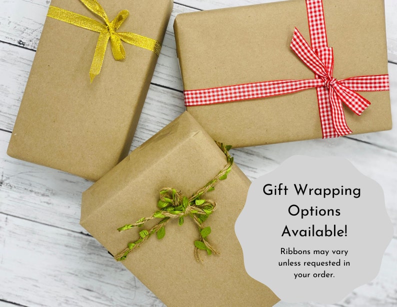 May include: Three brown paper gift boxes with different ribbon styles. The boxes are tied with a gold ribbon, a red and white gingham ribbon, and a brown twine ribbon with green leaves. The text on the image reads "Gift Wrapping Options Available! Ribbons may vary unless requested in your order."