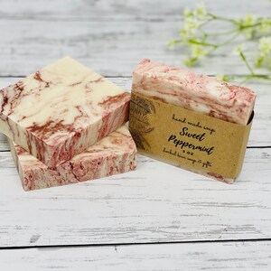 May include: Three bars of handmade soap with a marbled pink and white design. The top bar has a brown paper label that reads "hand made soap Sweet Peppermint 3 oz herbal kiwi soap & gifts".