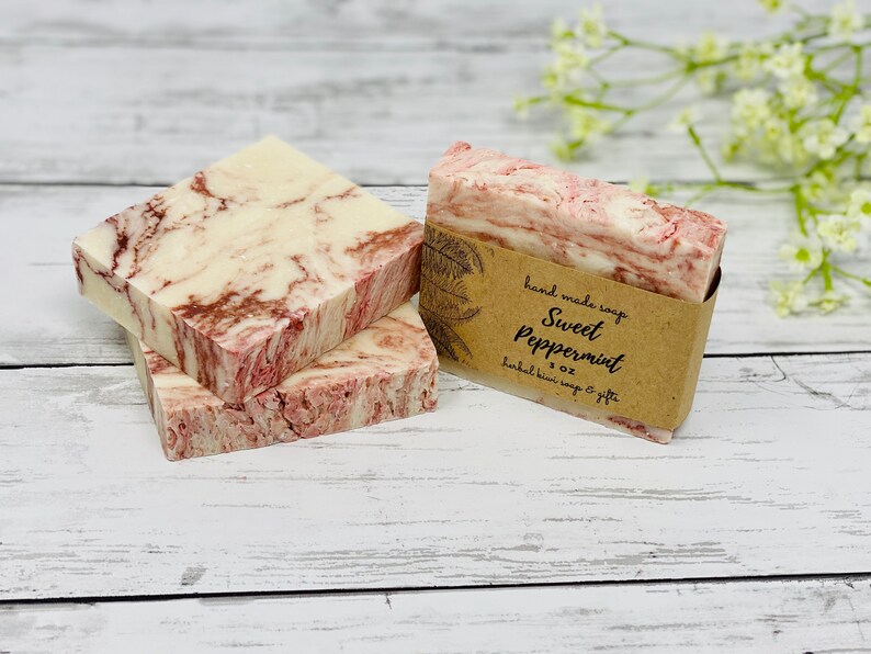 May include: Three bars of handmade soap with a marbled pink and white design. The top bar has a brown paper label that reads "hand made soap Sweet Peppermint 3 oz herbal kiwi soap & gifts".