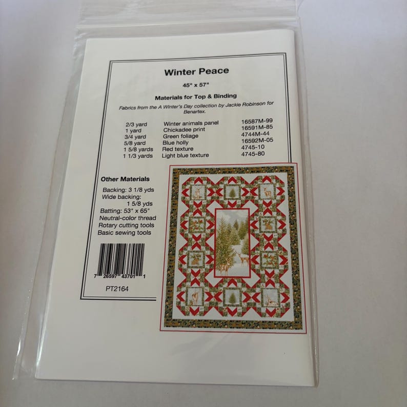 May include: A Winter Peace quilt pattern instruction sheet in a clear plastic sleeve. The document lists materials for a 114 cm by 145 cm quilt, including fabric requirements for winter animals, chickadees, foliage, and holly, with a barcode.