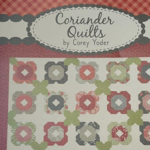 May include: A quilt pattern cover titled Coriander Quilts by Corey Yoder. The design features a repeating block pattern of floral and geometric shapes in shades of red, grey, and green on a white background, with a red patterned border.