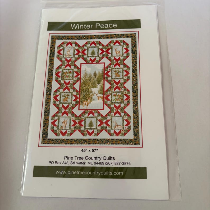 May include: A quilt pattern titled Winter Peace featuring a central panel of deer in a snowy forest surrounded by blocks of red and green geometric shapes and wildlife imagery. The pattern measures 45 inches by 57 inches and includes contact information for Pine Tree Country Quilts.