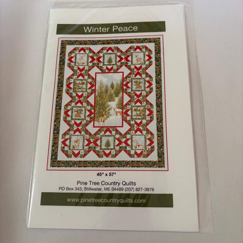 May include: A Winter Peace quilt pattern by Pine Tree Country Quilts measuring 45 inches by 57 inches. The design features a central panel of deer in a snowy forest surrounded by blocks with deer, trees, and holly, accented by red and white geometric shapes.