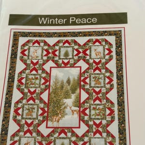 May include: A quilt pattern titled Winter Peace featuring a central rectangular panel of a snowy forest with deer, surrounded by a border of red and white geometric star blocks, green pine foliage, and small square vignettes of deer and birds.