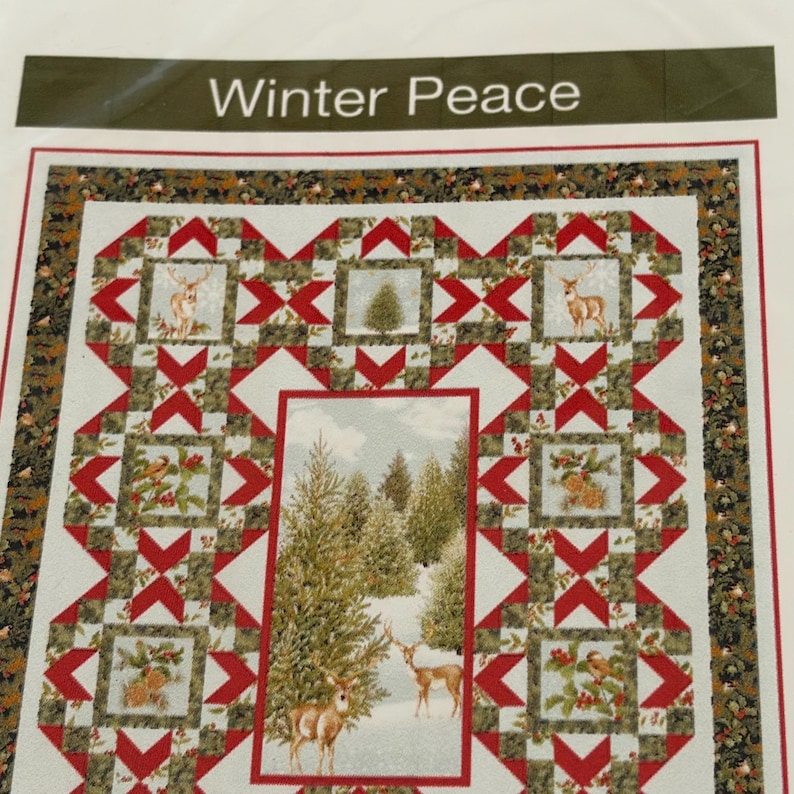 May include: A quilt pattern titled Winter Peace featuring a central rectangular panel of a snowy forest with deer, surrounded by smaller square blocks depicting deer, pine trees, and holly, all connected by red and green geometric star motifs.