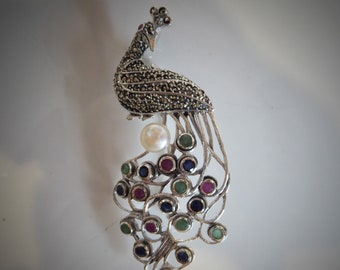 Puede incluir: Un broche de pavo real de plata con una perla y piedras preciosas de colores. El pavo real está decorado con piedras de marcasita negras.