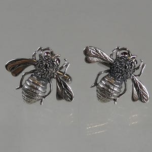 May include: A pair of silver bee cufflinks with a pink gemstone accent on each bee.