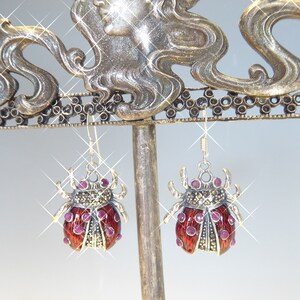 May include: A pair of silver earrings shaped like ladybugs with red enamel and pink gemstone accents.