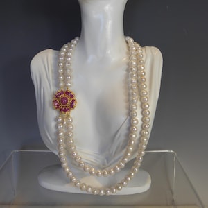 May include: A double strand pearl necklace with a gold and pink gemstone clasp. The necklace is displayed on a white mannequin.
