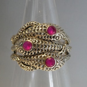 May include: A gold ring featuring three intertwined snake designs, each with a pink ruby gemstone in its eye.