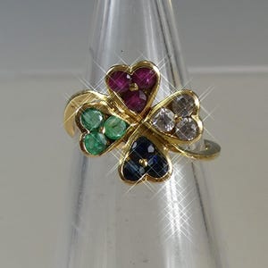 May include: A gold ring with a four-leaf clover design. The leaves are made of heart-shaped gemstones in ruby, emerald, sapphire, and clear crystal. The ring has a delicate band and a polished finish.