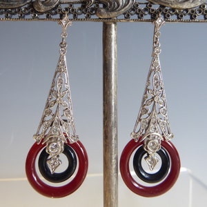 May include: A pair of silver dangle earrings with a geometric design and red and black stone accents.