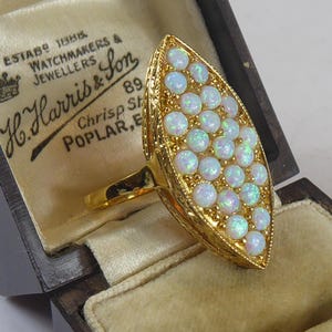May include: A gold ring with a teardrop-shaped setting filled with white opals. The ring is in a black velvet box with a label that reads "H. Harris & Son, Watchmakers & Jewellers, 89 Chrisp St, Poplar, E."