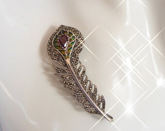 Puede incluir: Broche plateado con forma de pluma y detalles de marcasita. El broche presenta una piedra preciosa roja central y está adornado con esmalte verde y amarillo. El diseño de la pluma es detallado y elegante, adecuado para añadir un toque vintage a cualquier atuendo.