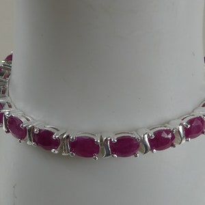 May include: A silver tennis bracelet with oval-shaped pink gemstones.