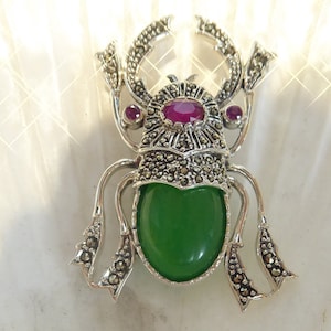 May include: A silver brooch in the shape of a beetle with a green stone cabochon and three pink stones. The beetle is detailed with marcasite.