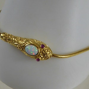 May include: A gold chain necklace with a white opal and two pink stones set in a gold snake-shaped pendant.