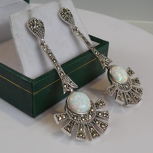 May include: A pair of silver dangle earrings featuring a white opal gemstone and marcasite accents. The earrings have a fan-shaped design.