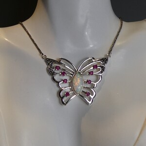 May include: Silver butterfly pendant necklace with an opal center stone and ruby accents. The butterfly design features openwork wings and a delicate chain. The necklace is displayed on a mannequin.