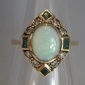 May include: A gold ring with a large white opal gemstone surrounded by smaller diamonds and green emeralds.