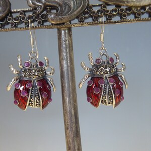 May include: A pair of silver earrings with a ladybug design. The ladybugs are red with black spots and have pink gemstones for eyes. The earrings are made with marcasite stones.