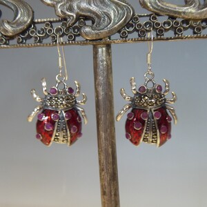 May include: A pair of silver earrings shaped like ladybugs with red enamel and purple gemstone accents.