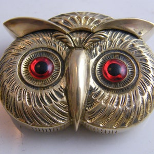 Peut inclure: Une figurine de hibou en laiton avec des yeux en verre rouge. Le visage du hibou est détaillé avec des lignes gravées et un bec proéminent.