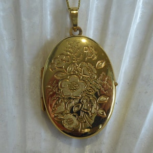 May include: A gold oval locket with a floral design. The locket has a hinge on the side and a loop at the top for a chain.