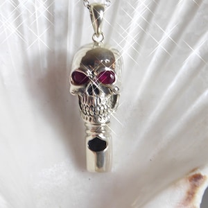 May include: Silver skull whistle pendant necklace with red gemstone eyes. The whistle is attached to the bottom of the skull.