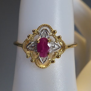 Puede incluir: Un anillo de oro con un rubí rojo y pequeños diamantes blancos engastados en un diseño delicado y ornamentado.