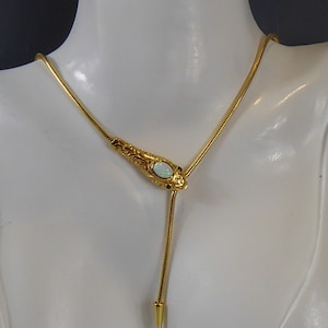 May include: A gold chain necklace with a pendant featuring a white opal stone set in a gold filigree design. The pendant is shaped like a snake's head with small black stones for eyes.