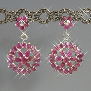May include: A pair of dangling earrings featuring a circular cluster of marquise-cut deep pink rubies arranged in a floral pattern. Each earring is suspended from a smaller, single five-petaled flower stud made of matching pink rubies.