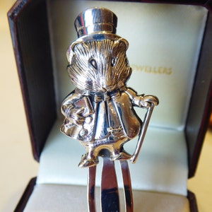 May include: Silver bookmark featuring a detailed figurine of a mouse wearing a top hat and holding a walking stick. The bookmark is in a velvet box.