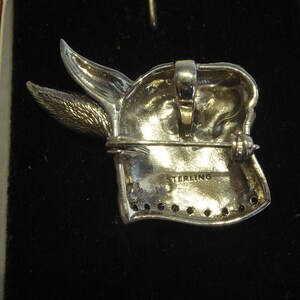 May include: Sterling silver brooch of a rabbit's head with a detailed design. The back of the brooch has a pin and clasp, and the words "STERLING" are stamped on the back.