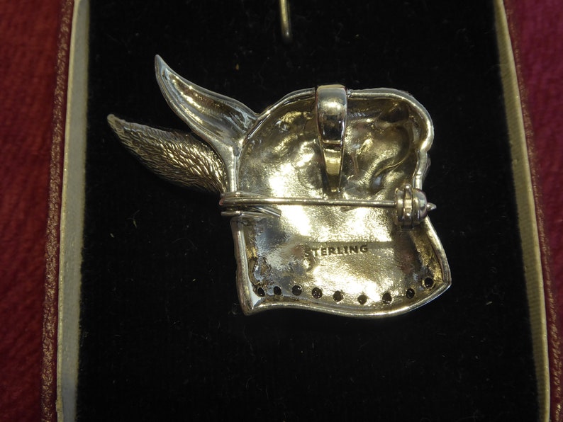 May include: Sterling silver brooch of a rabbit's head with a detailed design. The back of the brooch has a pin and clasp, and the words "STERLING" are stamped on the back.