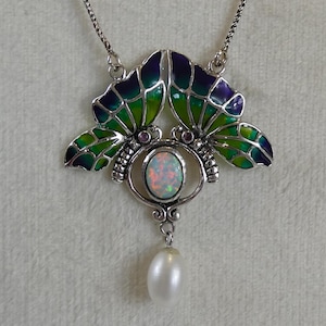 May include: A silver-toned necklace featuring a butterfly pendant with green and blue enamel wings. The pendant has an oval opal center and a dangling white pearl. The necklace is on a fine chain.