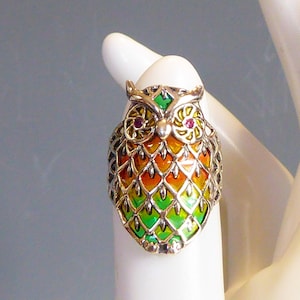 May include: A silver owl ring with green, orange and red enamel. The owl's eyes are set with red gemstones.